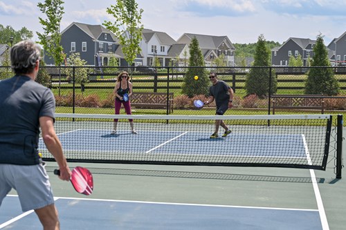 Residents playing pickleball on an outdoor community court with neighborhood homes in the background.