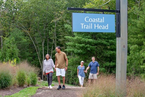 Active adults walking together at the Coastal Trail Head surrounded by trees and greenery.
