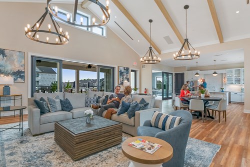 Bright community clubhouse interior with lounge seating, dining area, and residents relaxing under vaulted ceilings.